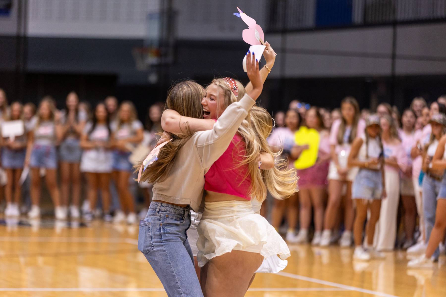 Two students hugging while a crowd of sorority members cheer behind them